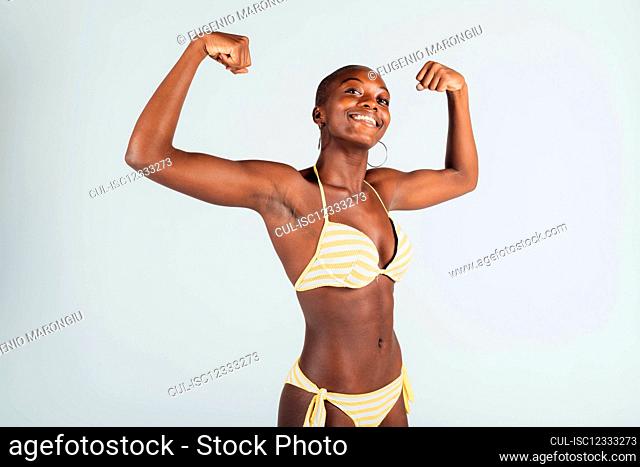 Young woman wearing bikini, flexing muscles