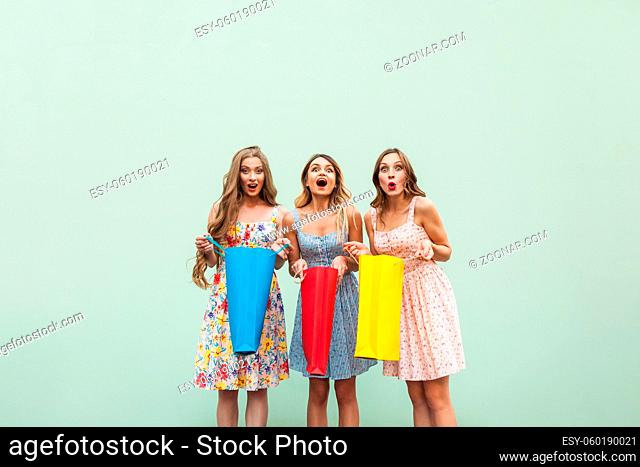 Three beautiful woman after shopping. Looking at camera, and wonder, because thay got gift from shop. Isolated on green background, studio shot