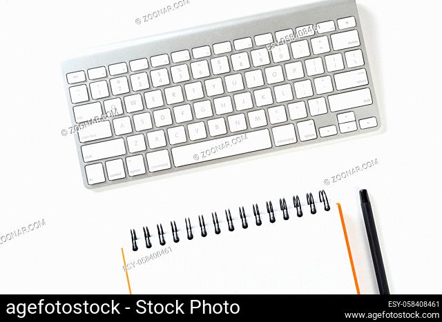 Top view of businessman workplace. Spiral notepad, pen and computer keyboard on white surface. Education, creativity and working concept with copy space