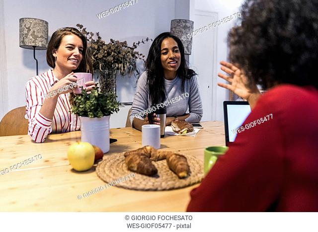 Three women with laptop talking at table