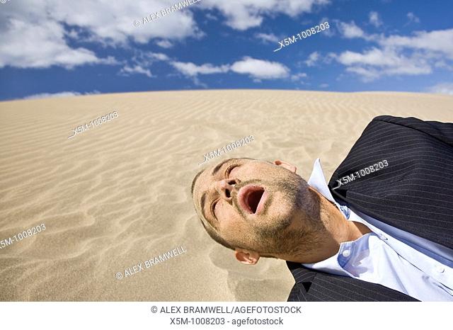 Businessman dying in the desert sun with sand all over his face