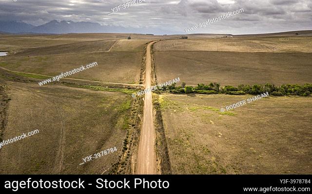 Aerial image of a rural, dusty, gravel road with recently harvested wheat fields on both sides of the road. A bare landscape