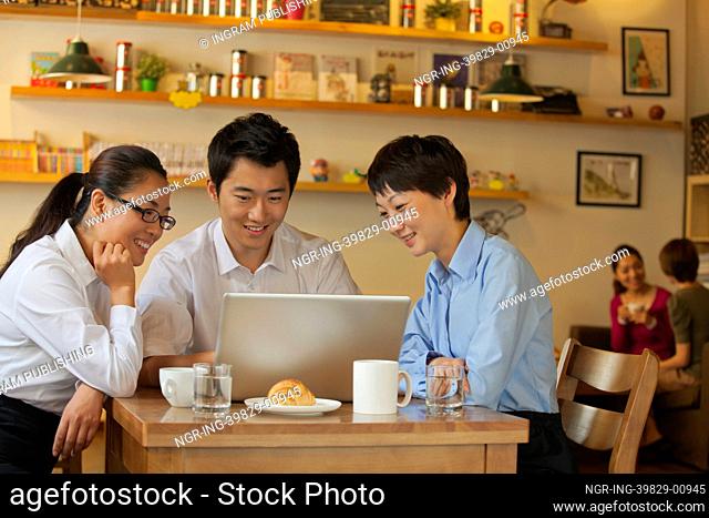 Three friends sitting in coffee shop, looking down at laptop