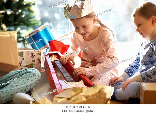 Girl and brother on living room floor gazing at toy guitar christmas gift