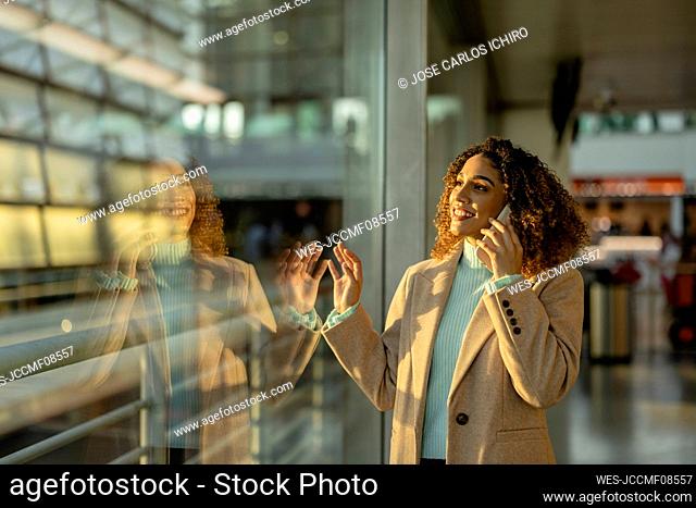 Happy woman talking on mobile phone by glass window at station