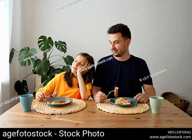 Tired girl with father having breakfast on dining table