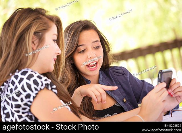 Expressive young adult girlfriends using their smart cell phone outdoors
