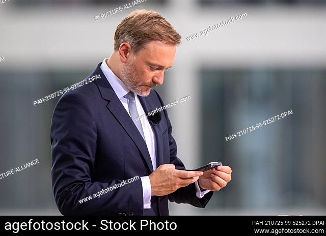 25 July 2021, Berlin: Christian Lindner, party leader of the FDP, looks at his smartphone during the ARD summer interview on the terrace of the...