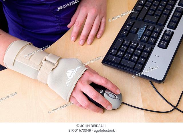 Office worker using a computer mouse whilst wearing an elasticated wrist support to help alleviate repetitive strain injury RSI