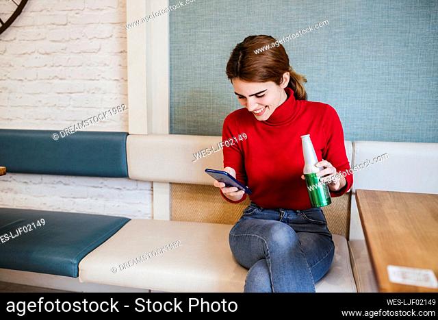 Happy woman using smart phone while having beer in bar