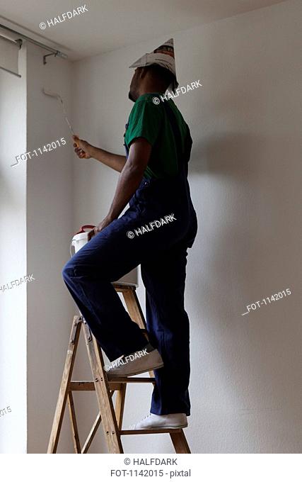 A man standing on a ladder and painting a wall