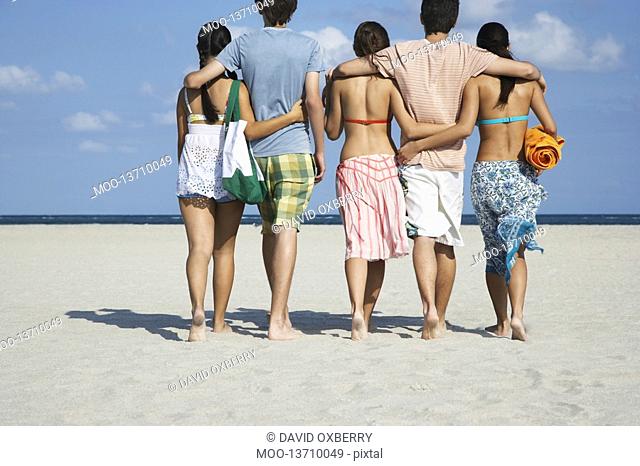 Group of teenagers 16-17 walking on beach back view