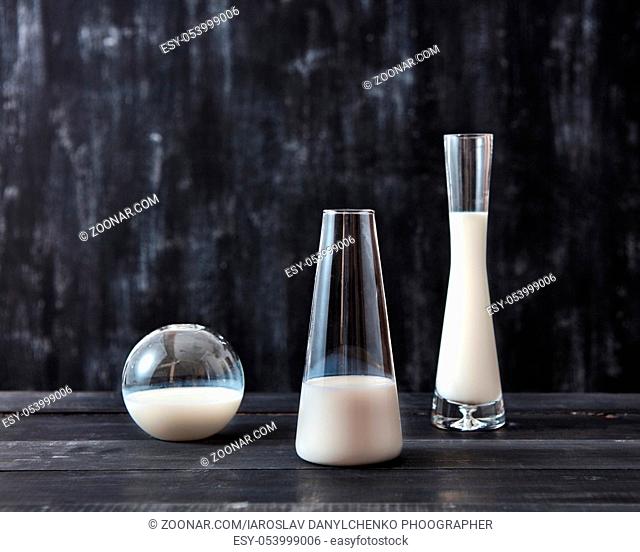 White milk in the glass vases on a dark wooden table on a back with copy space. Milk saving concept