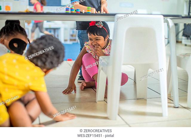 Cheerful girls playing under the table in kindergarten