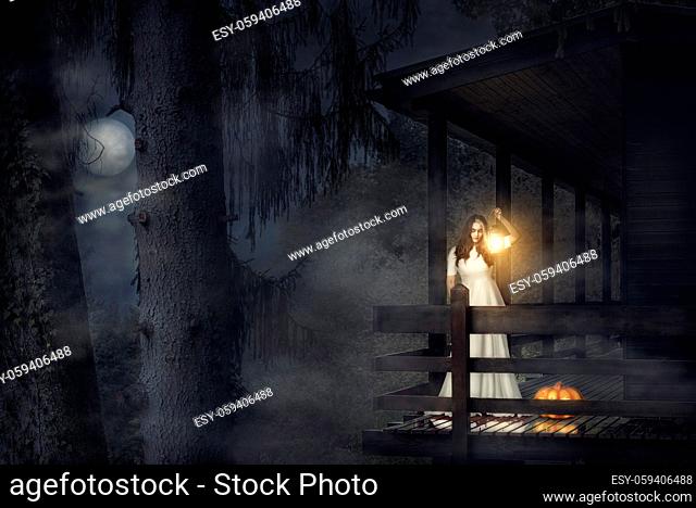 Spooky girl, in a white dress, holding a lit lantern, a pumpkin near her, on the balcony of a wooden house, in a dark foggy forest, under the moonlight