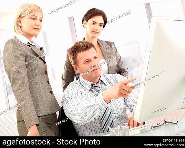Business team in office, businessman pointing at computer, businesswomen looking at screen