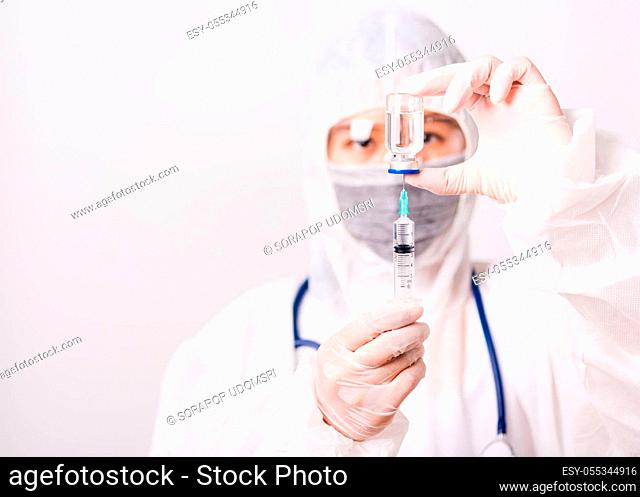 Asian female woman doctor or nurse in PPE uniform and gloves wearing face mask protective in the laboratory holding needle syringe drug and medicine vial...