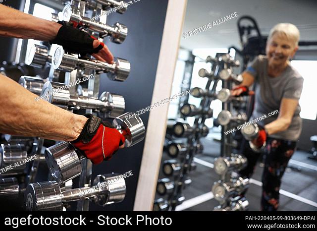 05 April 2022, North Rhine-Westphalia, Cologne: Model Elke takes weights from the rack at the Holmes Place gym. The Fibo fitness trade show will be held in...
