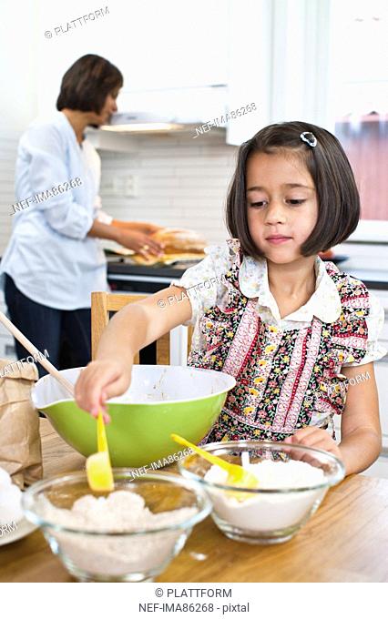 Girl baking in kitchen with mother in background
