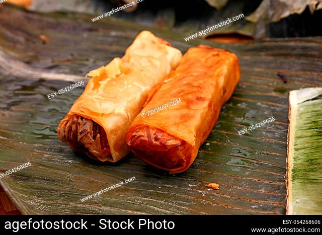 Portion of two deep fried crispy spring rolls, traditional Asian cuisine appetizer snack, served on green banana leaves, high angle view