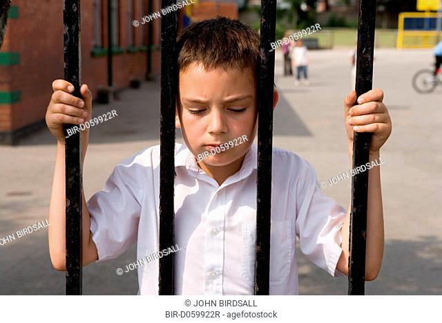 Boy looking through the fence out of the school playground