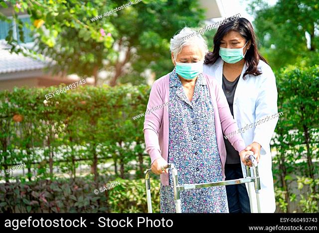 Doctor help Asian senior or elderly old lady woman walk with walker and wearing a face mask for protect safety infection and kill Novel Coronavirus Covid-19...