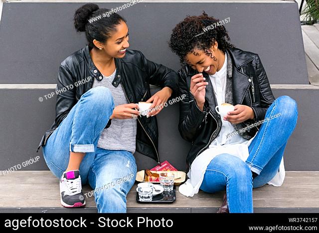 Two north African teen friends drinking together coffee outside