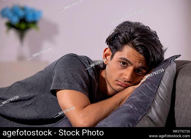 Close-up portrait of teenage boy leaning on sofa at home