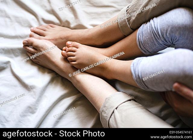 Close up of a mother and child's feet rubbing together while sitting on some beige bed sheets. It's a tender intimate moment
