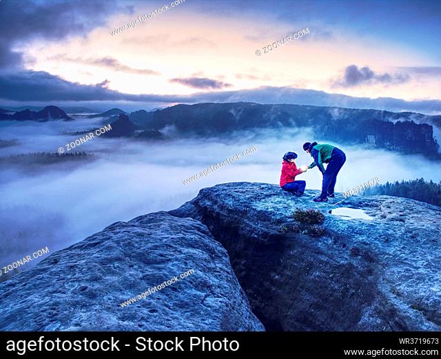 Night photo A woman shows magical lightning lantern to her man. Woman sits on a rock and shines to misty darkness. First Sun rays appear in the clouds