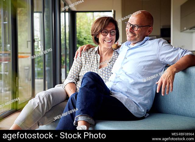 Cheerful senior woman with man sitting on sofa together at home