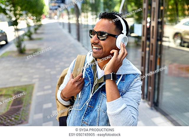indian man in headphones with backpack in city