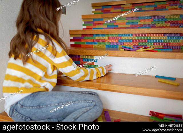 Rear view of girl sitting on stairs and playing with wooden blocks