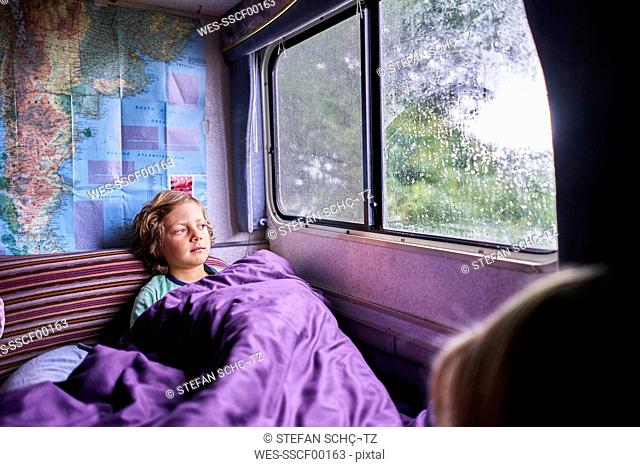 Boy in pyjama looking out of window of a camper