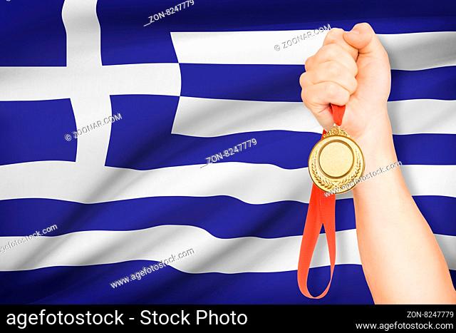 Sportsman holding gold medal with flag on background - Hellenic Republic