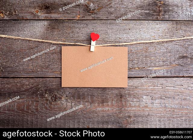 Valentines day card hanging on pin with heart on rope over wooden background, copy space for text