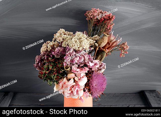 Still life image of dried flowers in rustic vase against weathered wooden background