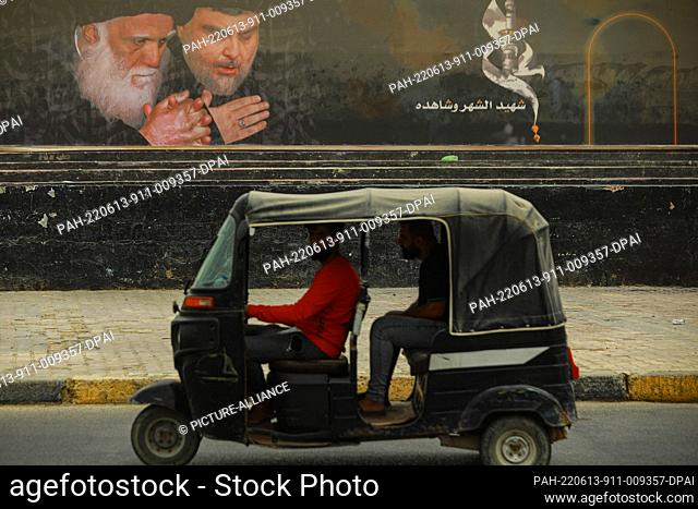 13 June 2022, Iraq, Sadr City: A man drives his tuk-tuk past a poster bearing the image of Iraqi Shia cleric Muqtada al-Sadr