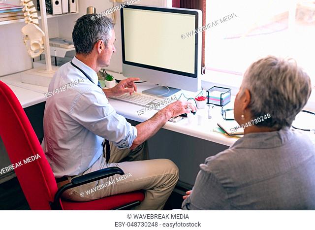 Male doctor discussing over computer with senior woman