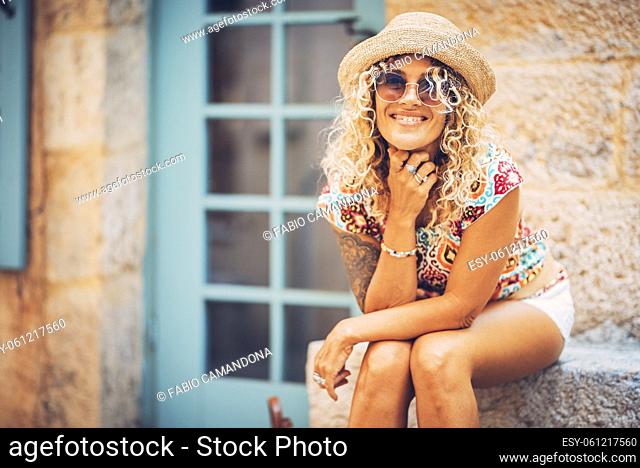 Portrait of beautiful smiling hipster young woman in sunglasses and straw hat sitting outdoors on a bright sunny day. Stylish tattooed woman in good mood...
