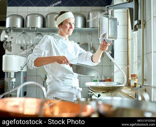Happy young confectioner measuring sugar on scale in kitchen