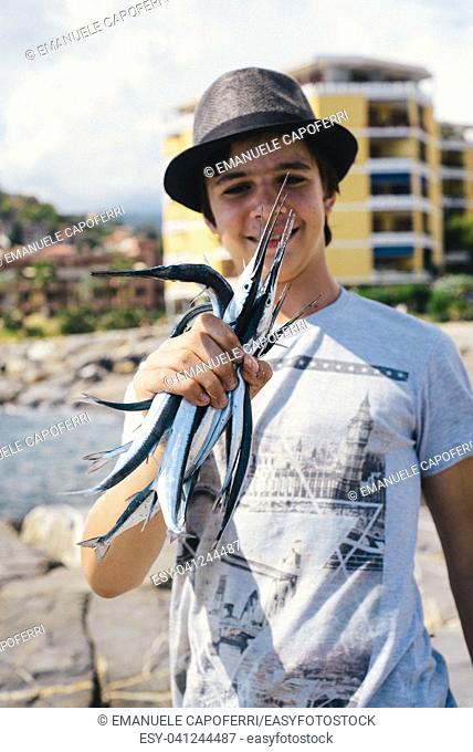 portrait of a fisherman boy holding a group of freshly-drawn garfish in the sea of Liguria