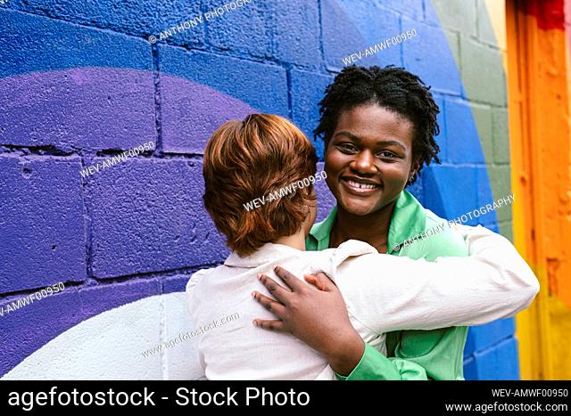 Smiling woman embracing friend by colorful wall