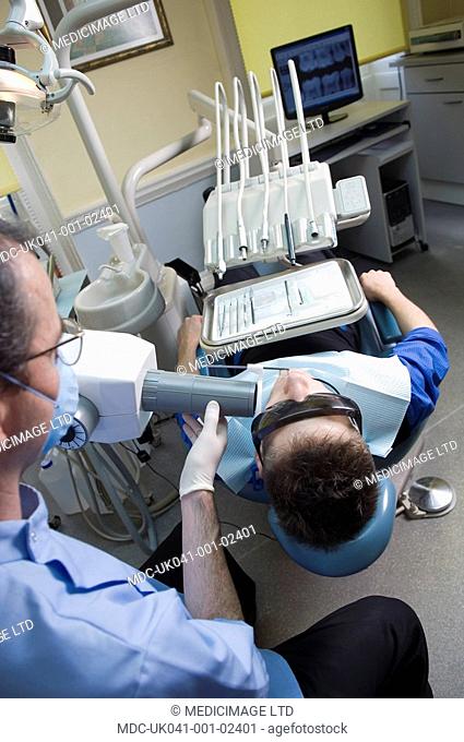 Dentist wearing safety glasses and mouth mask xrays the teeth of young male patient, also wearing special protection glasses