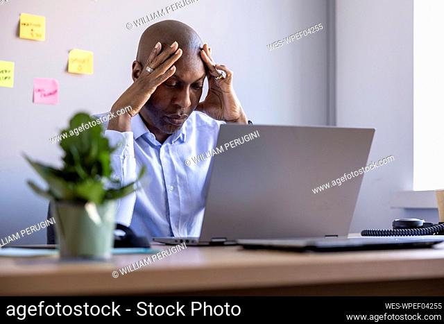 Worried male entrepreneur sitting with laptop at office