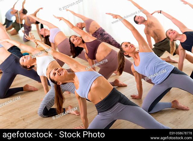Group of young sporty attractive people in yoga studio, practicing yoga lesson with instructor, sitting on floor in Padmasana, lotus meditative yoga pose