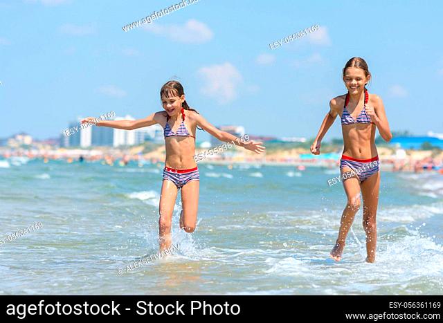 Two girls joyfully run along the seashore on a warm summer day