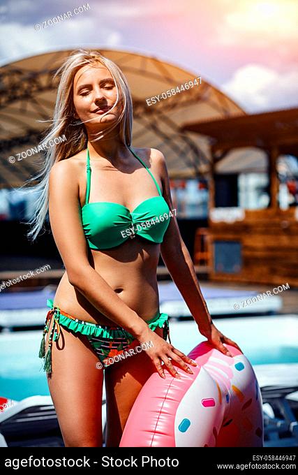 Beautiful lovely pretty woman with ash-blond hair in an inflatable floating ring in the form of a donut near the swimming pool looking at the camera