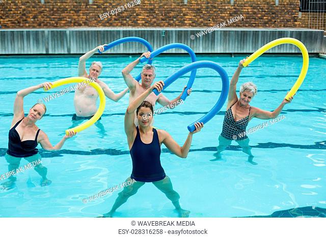 Trainer and senior swimmers exercising with pool noodle