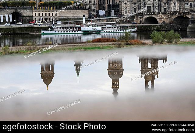 03 November 2023, Saxony, Dresden: The towers of the Ständehaus (l-r), the Georgentor, the Hausmannsturm and the Hofkirche are reflected in a puddle on the...